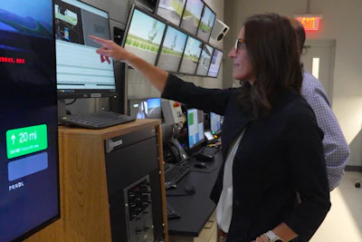 Woman pointing at security monitoring station with multiple display screens and control equipment in command center