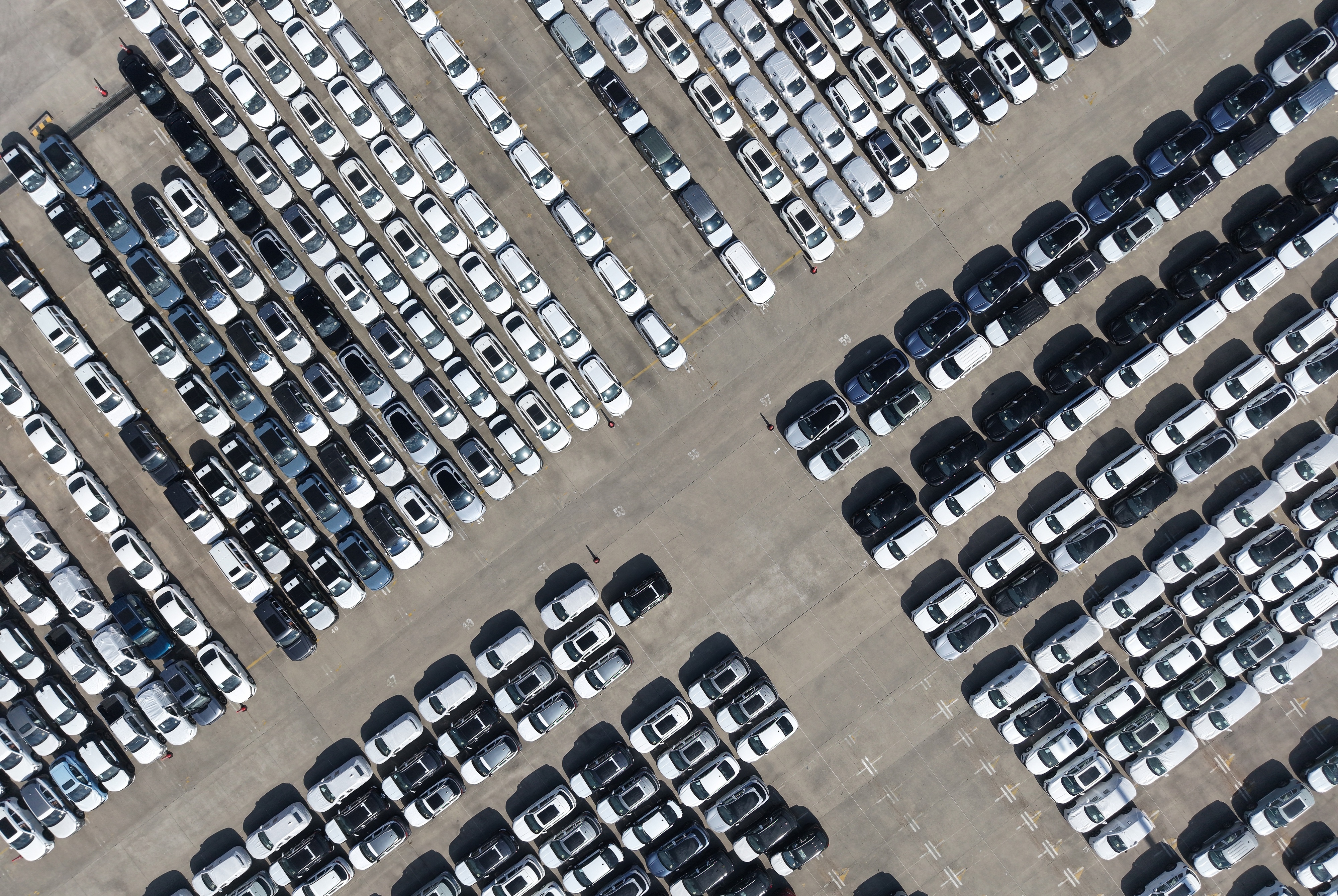 Aerial view of a large parking lot with hundreds of white, gray, and black vehicles arranged in organized rows