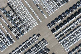 Aerial view of a large parking lot with hundreds of white, gray, and black vehicles arranged in organized rows