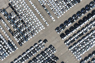 Aerial view of a large parking lot with hundreds of white, gray, and black vehicles arranged in organized rows