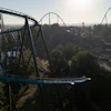 Aerial view of blue roller coaster tracks winding through an amusement park surrounded by trees and landscape