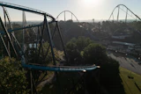 Aerial view of blue roller coaster tracks winding through an amusement park surrounded by trees and landscape