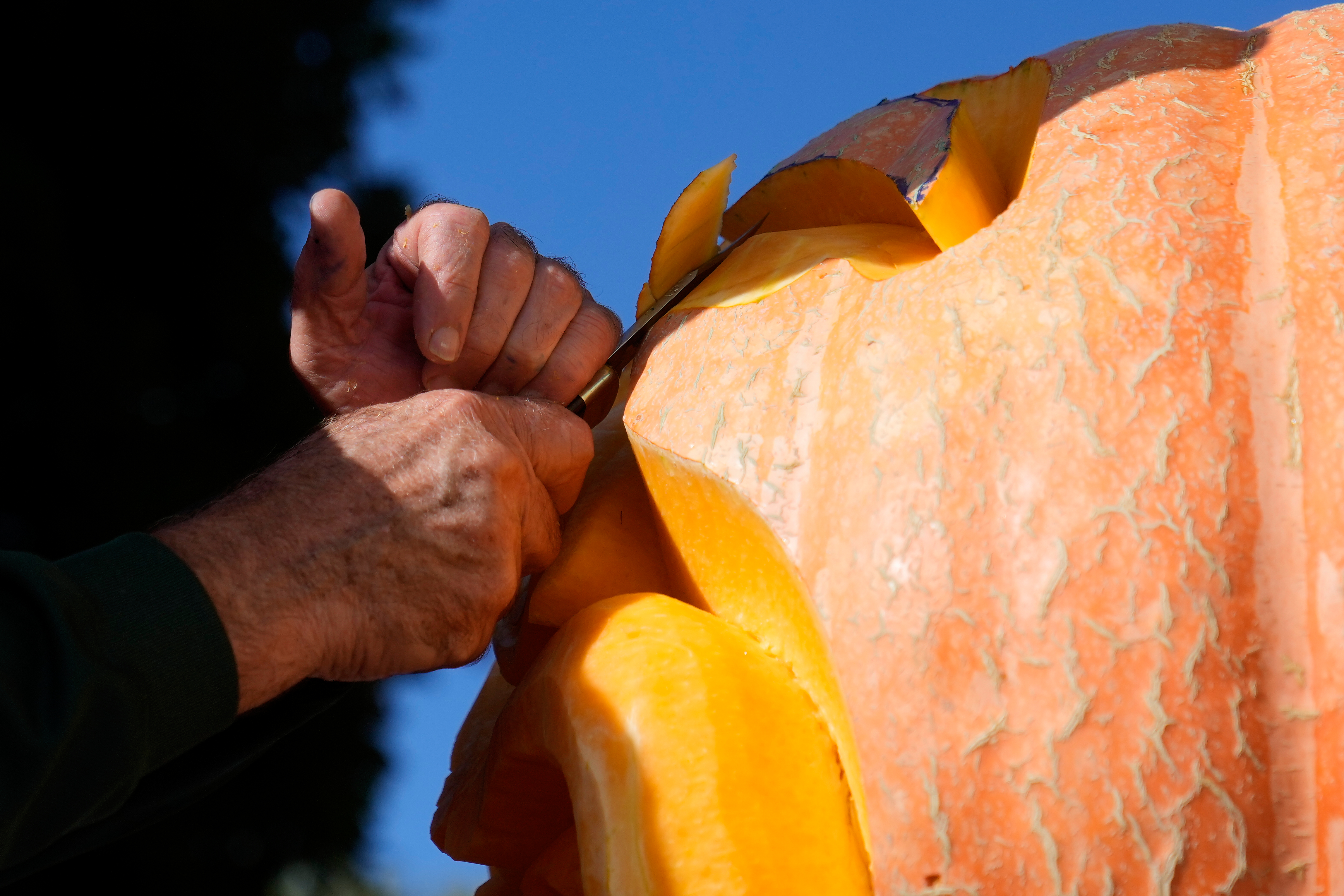Person's hand gripping an orange and yellow metal object against a clear blue sky