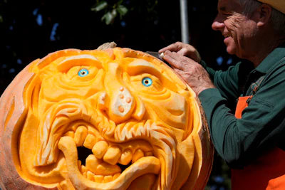 Intricately carved jack-o'-lantern pumpkin with detailed facial features and blue eyes, held by a person in a green shirt