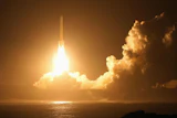 Rocket launching at night with bright engine flames piercing through golden clouds over the ocean
