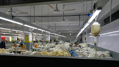 Industrial textile factory floor with workers processing fabrics at production stations under bright overhead lighting
