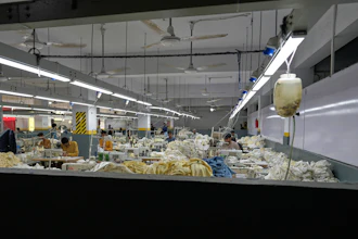 Industrial textile factory floor with workers processing fabrics at production stations under bright overhead lighting