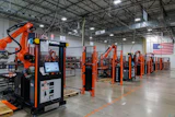 Industrial robotic welding facility with orange automation equipment and American flag in warehouse setting