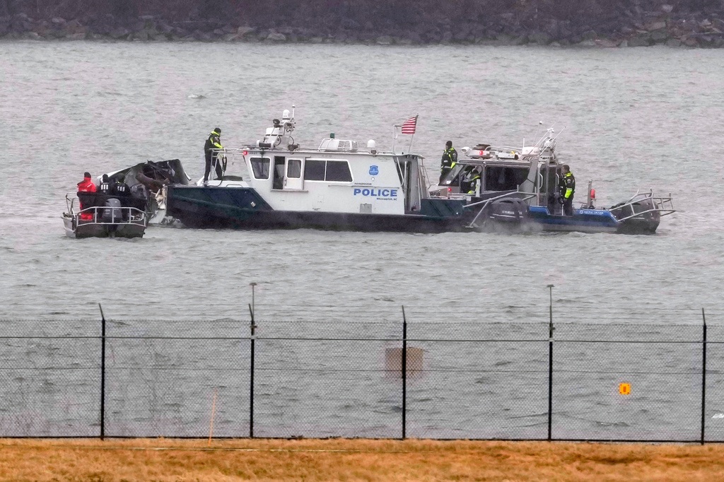 Police boat with personnel conducting water rescue operations near shoreline barrier