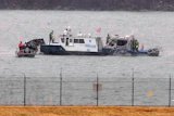 Police boat with personnel conducting water rescue operations near shoreline barrier
