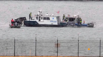 Police boat with personnel conducting water rescue operations near shoreline barrier