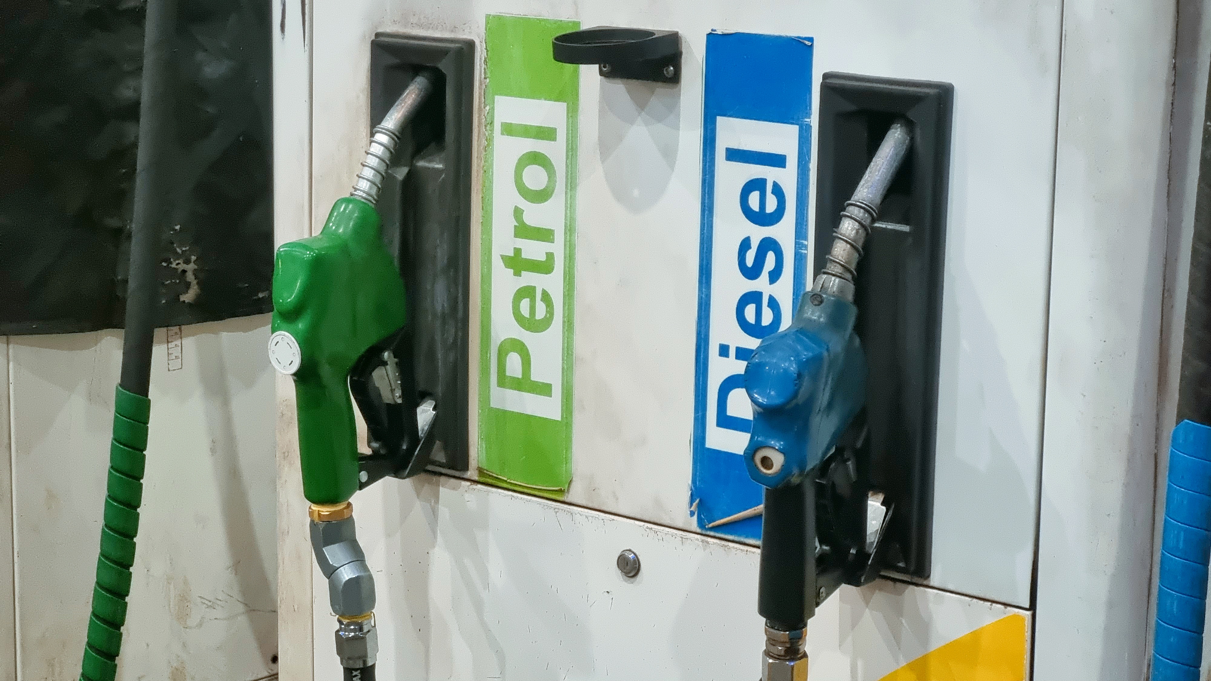 Green and blue fuel pump nozzles labeled Petrol and Diesel at a gas station dispenser