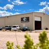 Surveying & Scale industrial warehouse building with metal siding and parked vehicles in desert landscape