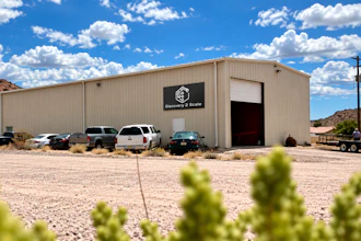 Surveying & Scale industrial warehouse building with metal siding and parked vehicles in desert landscape