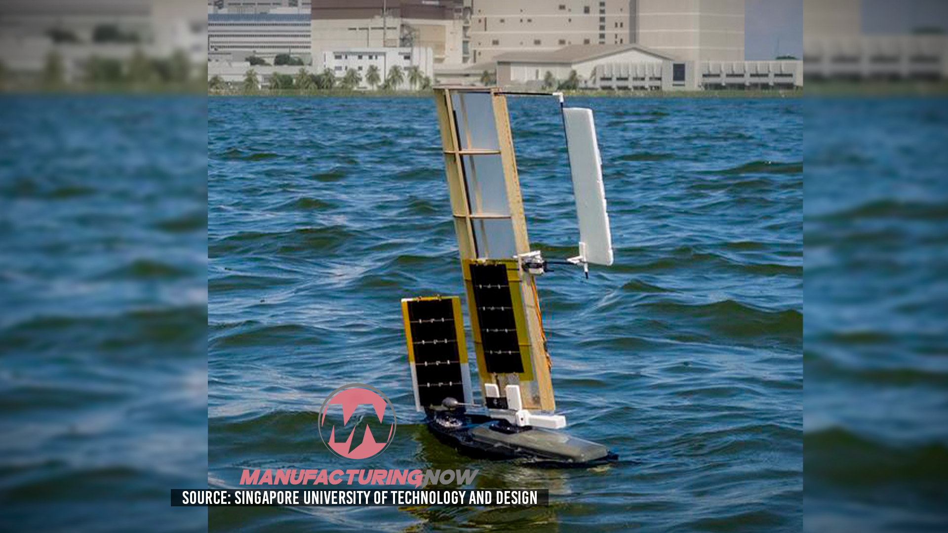 Autonomous solar-powered sailboat with white sails on blue water near waterfront buildings