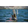 Autonomous solar-powered sailboat with white sails on blue water near waterfront buildings