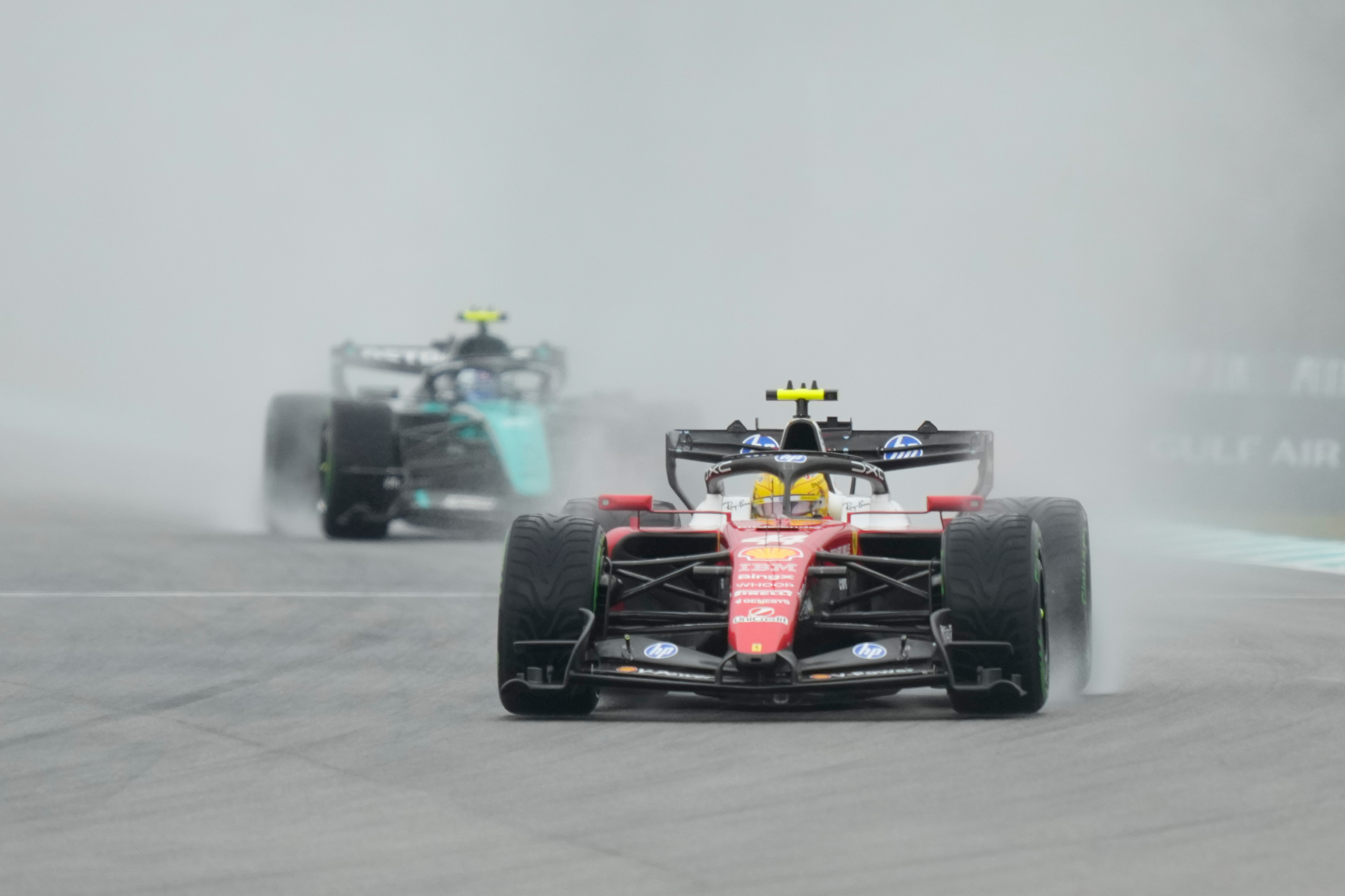 Formula 1 racing cars competing on a wet track in rainy conditions, with red and black vehicles leading the field.