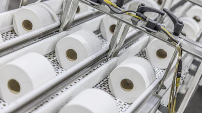 Industrial production line with multiple white tissue paper rolls on conveyor system with mechanical components and yellow wiring