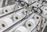 Industrial production line with multiple white tissue paper rolls on conveyor system with mechanical components and yellow wiring