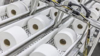 Industrial production line with multiple white tissue paper rolls on conveyor system with mechanical components and yellow wiring