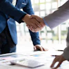 Two business professionals shaking hands over documents during a corporate meeting in a bright office setting