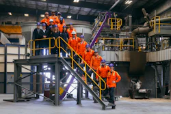 Industrial facility tour with group in orange safety uniforms on yellow metal stairs and platforms