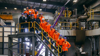 Industrial facility tour with group in orange safety uniforms on yellow metal stairs and platforms