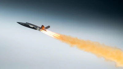 Fighter jet in flight with afterburners creating orange flame trail against blue sky