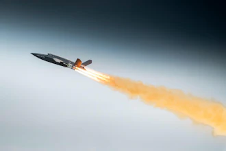 Fighter jet in flight with afterburners creating orange flame trail against blue sky