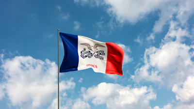 Iowa state flag waving on a flagpole against a blue sky with white clouds