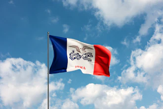 Iowa state flag waving on a flagpole against a blue sky with white clouds