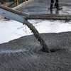 Concrete being poured from a chute during construction work on a wet surface