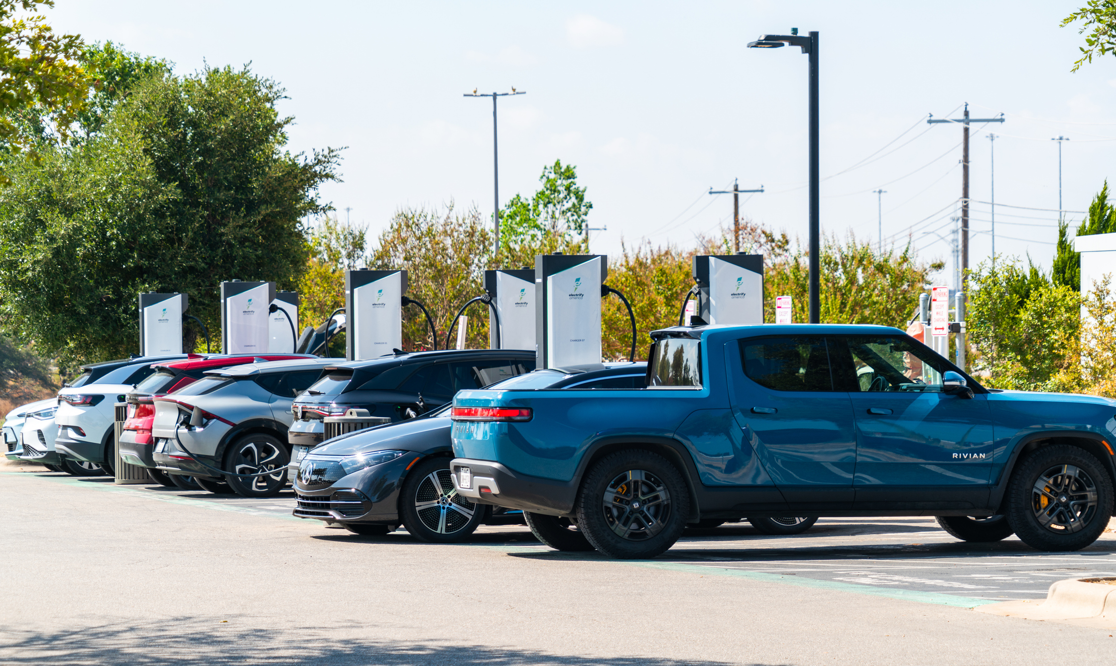 Row of electric vehicles charging at outdoor station with multiple chargers