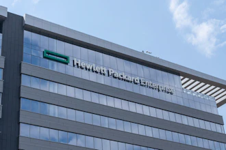 Modern glass and steel office building with company signage on facade under blue sky