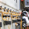 Electrician installing yellow wiring in industrial circuit breaker panel with safety gloves