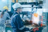 Industrial worker in hard hat using AR technology displaying AI analytics and data metrics on holographic display in manufacturing facility