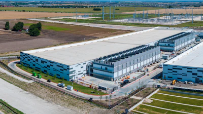 Aerial view of modern industrial warehouse complex with blue-accented buildings, loading docks, and surrounding agricultural landscape.
