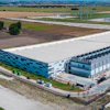 Aerial view of modern industrial warehouse complex with blue-accented buildings, loading docks, and surrounding agricultural landscape.