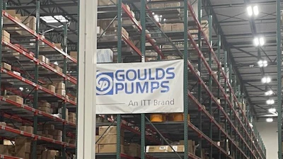 Industrial warehouse interior with tall storage racks, branded signage including Goulds Pumps and Rexnord logos, pallets, and orange safety markers on concrete floor.