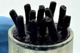 Black rod-like structures in clear cylindrical container against blue background