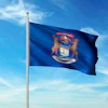 Michigan state flag waving on a flagpole against a blue sky with white clouds