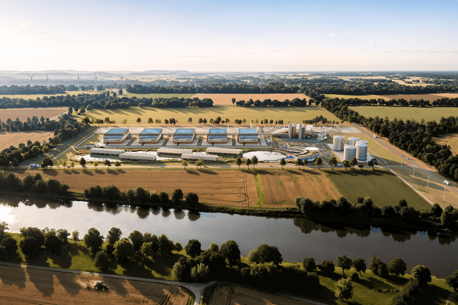 Aerial view of industrial facility with blue-roofed buildings, storage tanks, and surrounding agricultural fields near a river