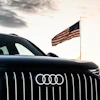Black Audi vehicle with American flag at sunset