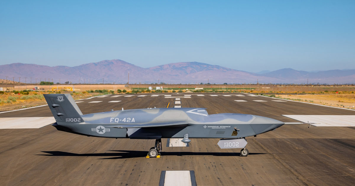 Gray RQ-4 Global Hawk military drone aircraft parked on desert runway with mountains in background