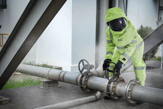 Industrial worker in neon safety gear adjusting valve on large metal pipeline system