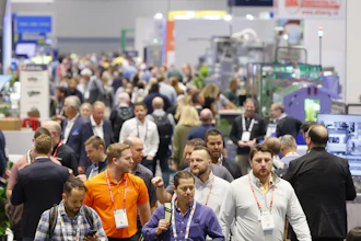 Crowded trade show floor with attendees wearing lanyards and ID badges networking among exhibition booths