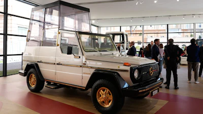 Vintage Mercedes-Benz G-Class with white body and gold wheels displayed in modern showroom with visitors