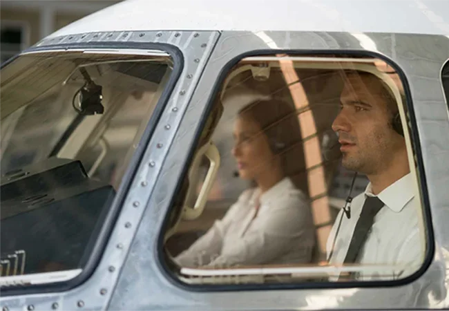 Two people seated in vintage aircraft cabin with sunlight streaming through windows