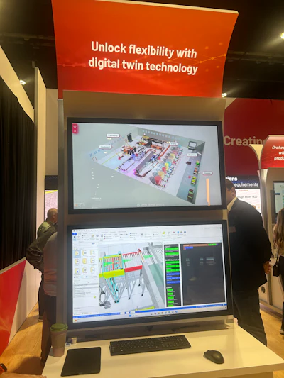 Trade show booth displaying digital twin technology with dual monitors showing 3D factory simulation and CAD software interface