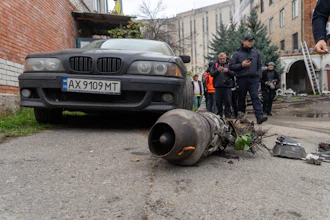 Damaged BMW sedan with detached engine component displayed on ground during investigation with officials and onlookers in urban courtyard